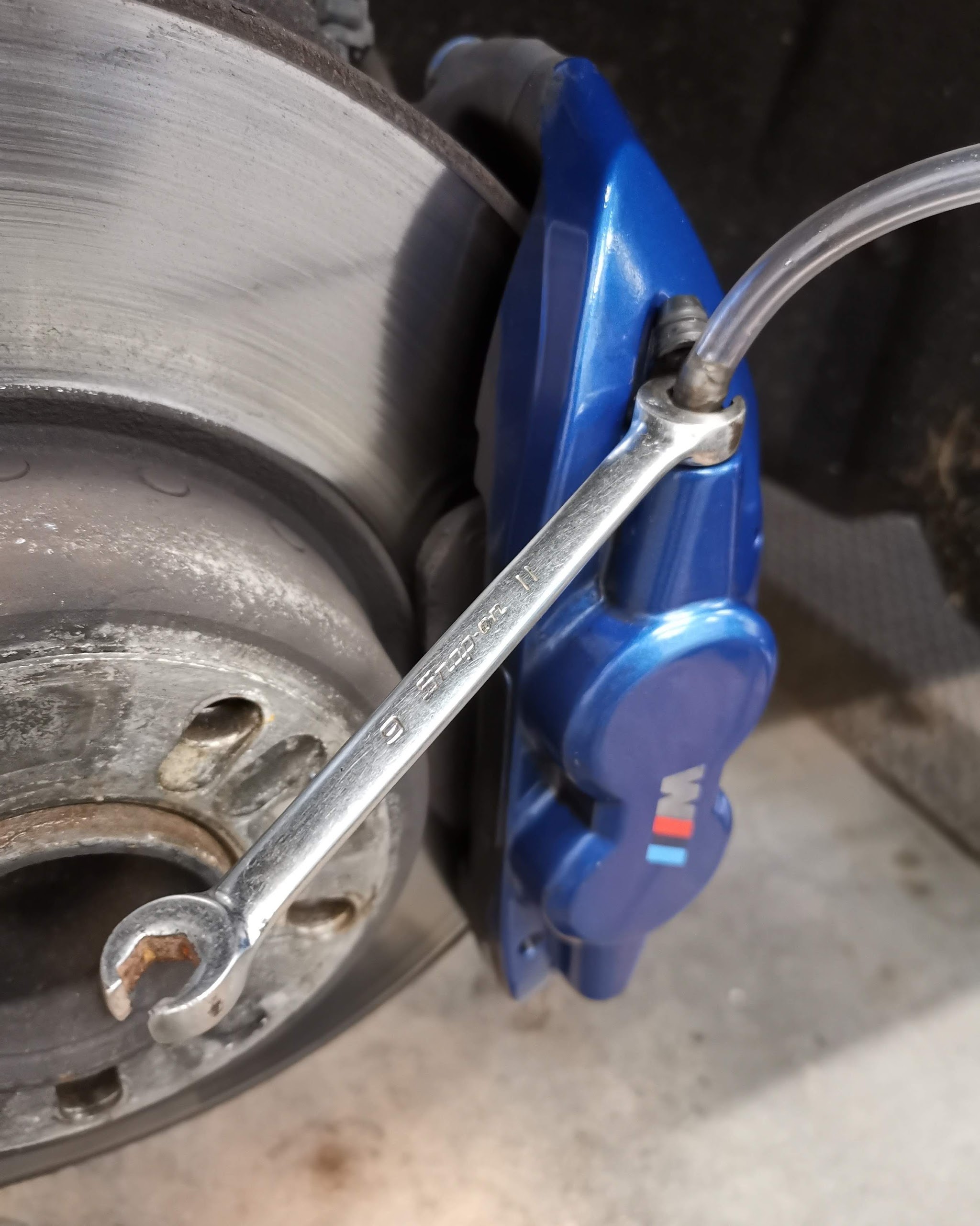 A spanner on the bleed nipple of a blue brake caliper with a clear bleed tube attached