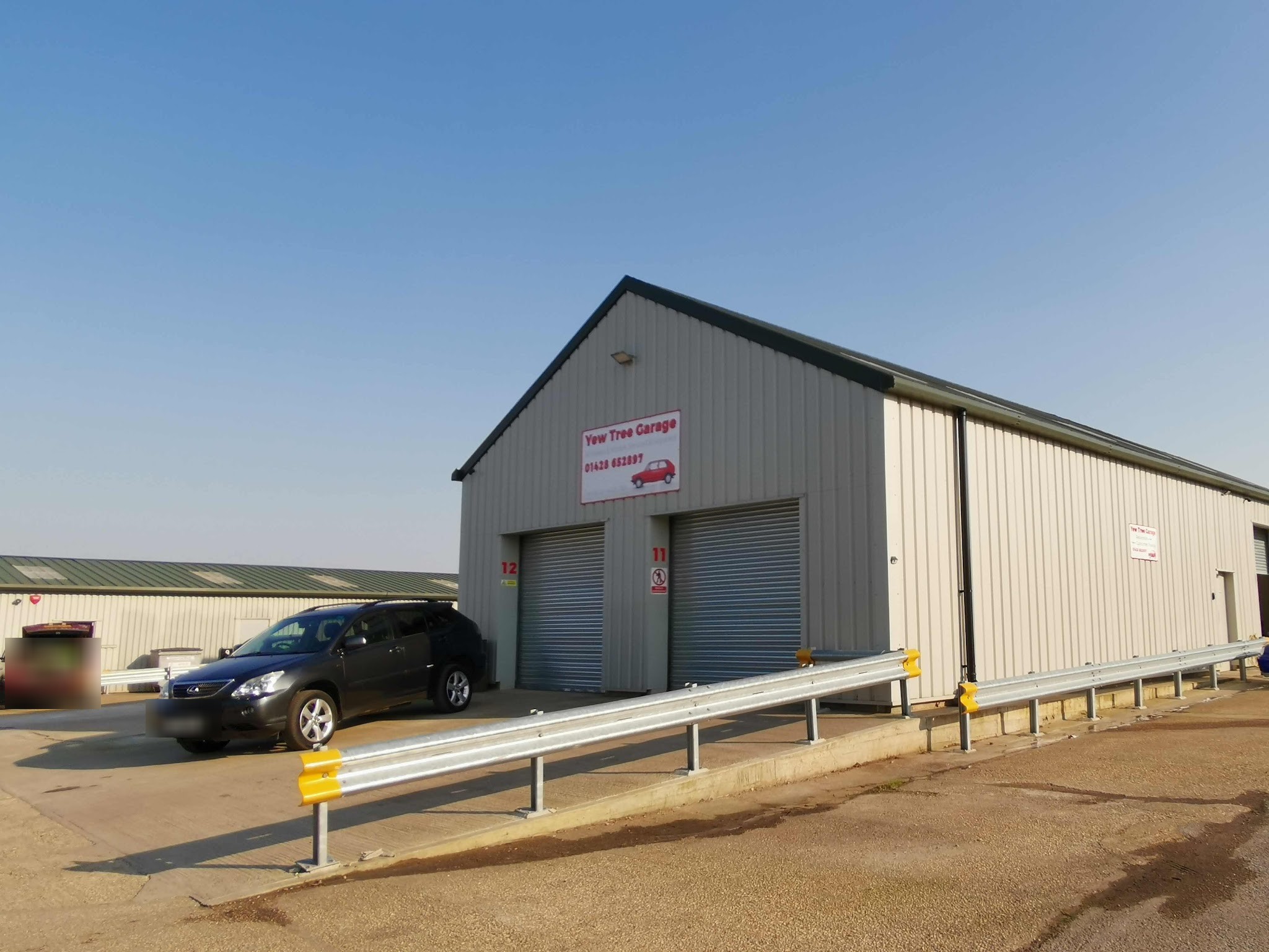 The Yew Tree Garage building from the yard on a clear day: a grey clad unit with two roller doors and the red and white sign above them